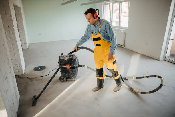 Male worker cleaning floor with vacuum cleaner. Electrical drill equipment on laminate. Cleaning service. Renovation and construction site concept