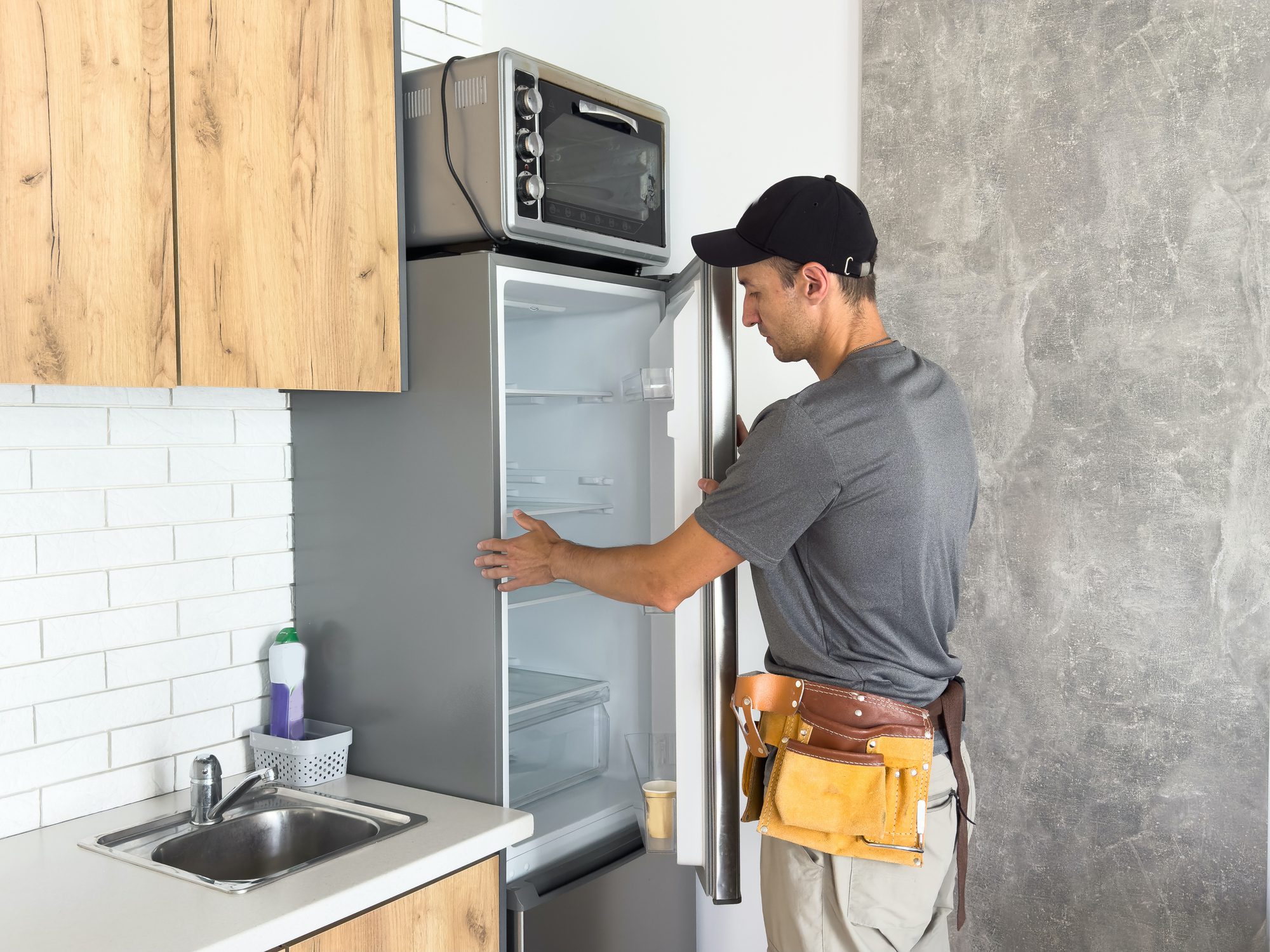 Male technician with screwdriver repairing refrigerator indoors. High quality photo