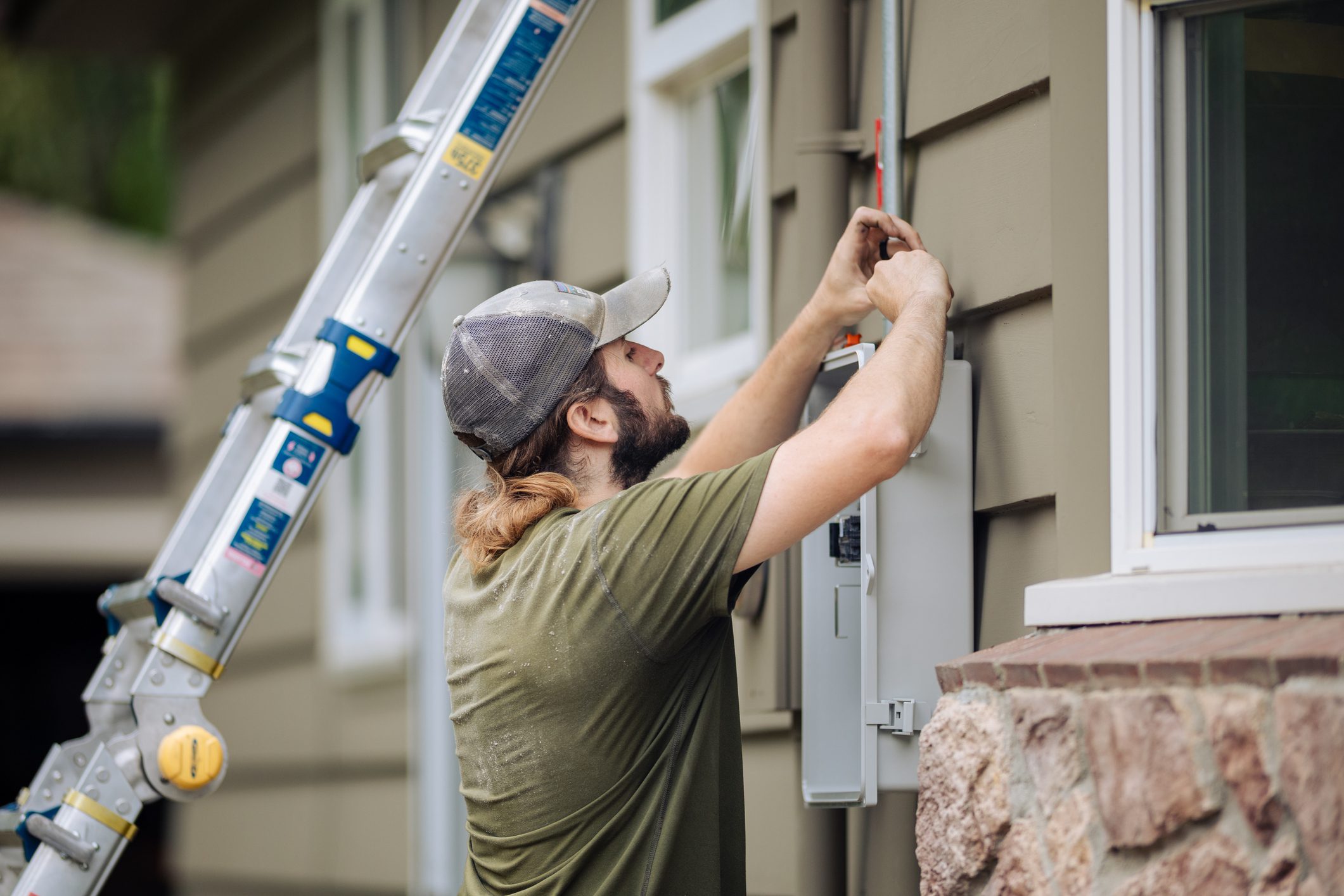 A professional solar technician installing a Solar Panel Electric Box on the side of a house