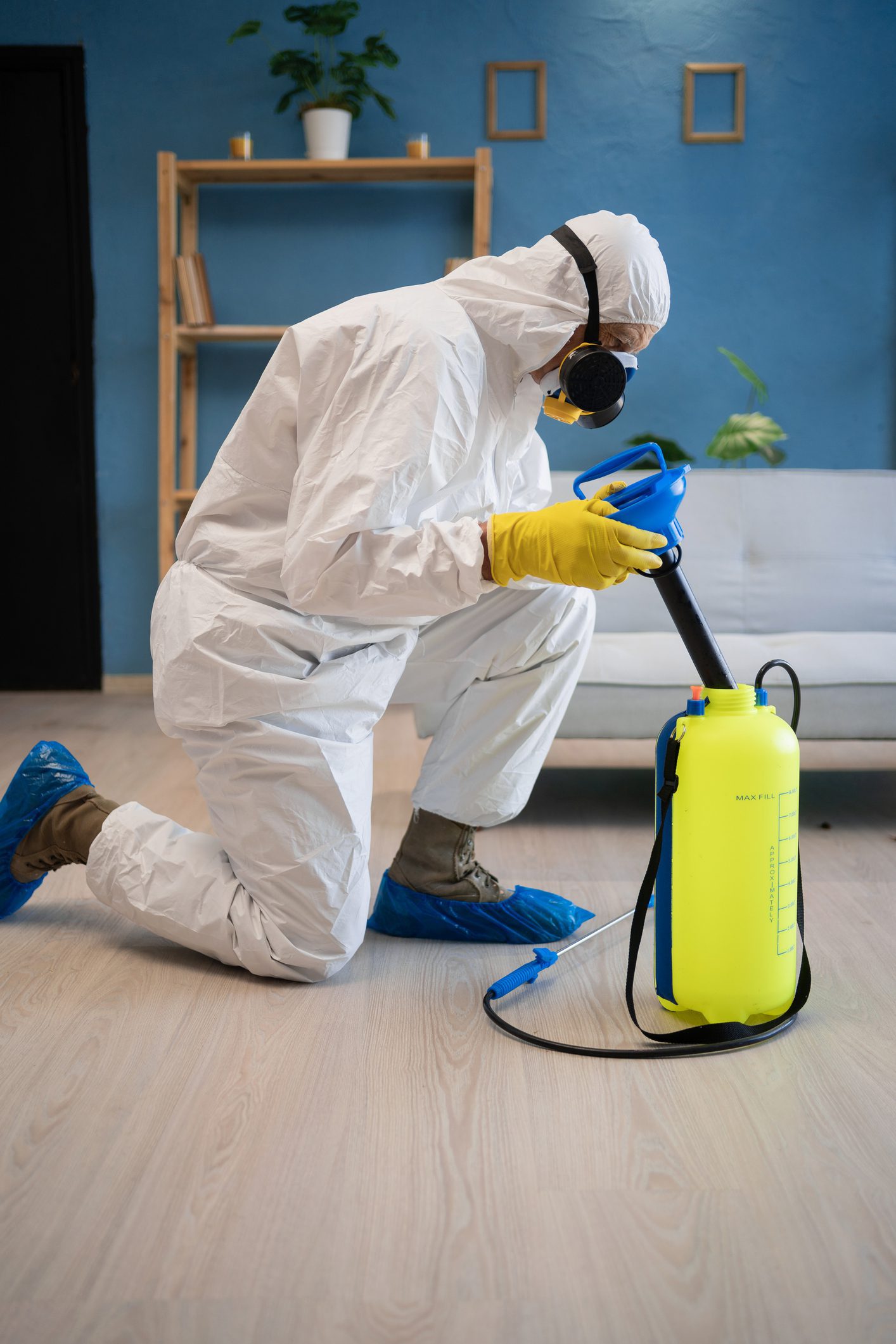 Pest control exterminator in white protective suit, mask and gas respirator with sprayer equipment killing cockroaches in apartment or house on the floor. copy space